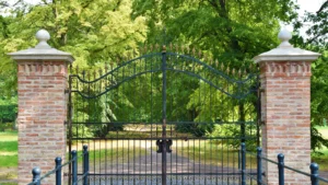 Black metal driveway gates surrounded by mature green trees